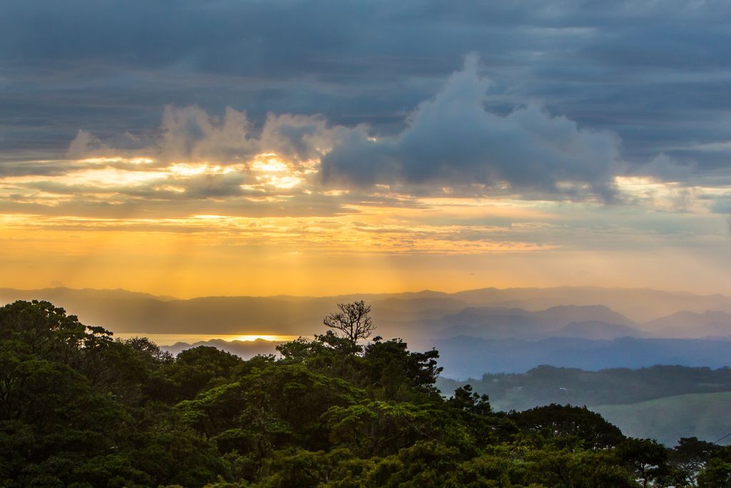 Light pouring through clouds, with the rainforest landscape below